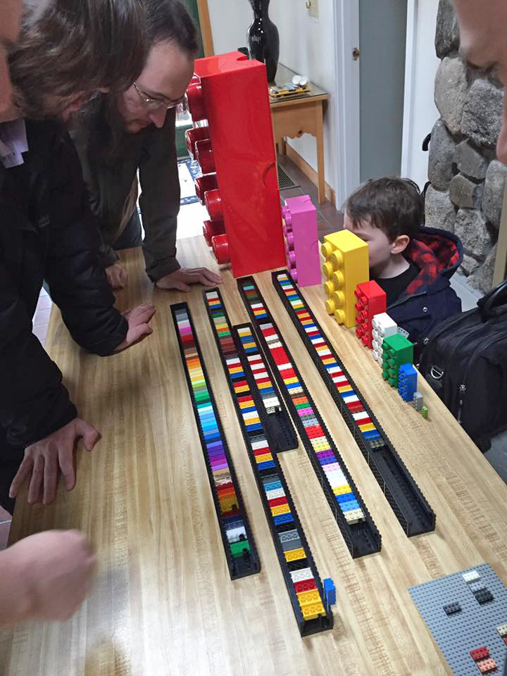 members leaned over to study an organized collection of colorful 2x4 bricks.